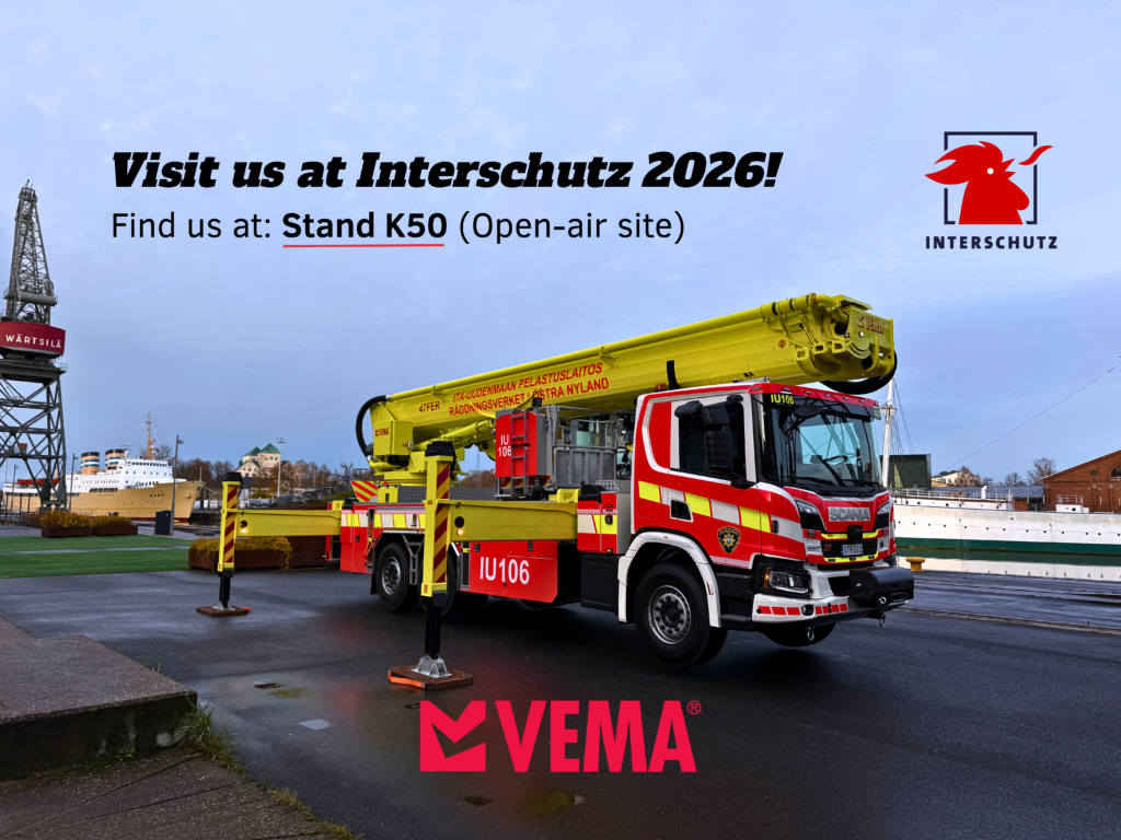 A Vema aerial firefighting platform is positioned outdoors near a waterfront under a cloudy sky. The extended boom is mounted on a Scania chassis, with stabilizers deployed. In the background, an industrial harbor scene is visible. Text on the image invites visitors to Interschutz 2026 in Hanover, Germany, with details to find Vema at Stand K50 (Open-air site). The Vema logo appears at the bottom, and the Interschutz logo is shown in the top right corner.